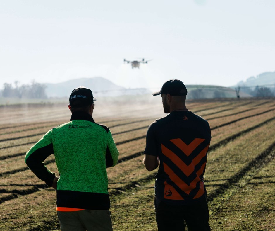 Two operators watching a spray drone work over a cultivated paddock