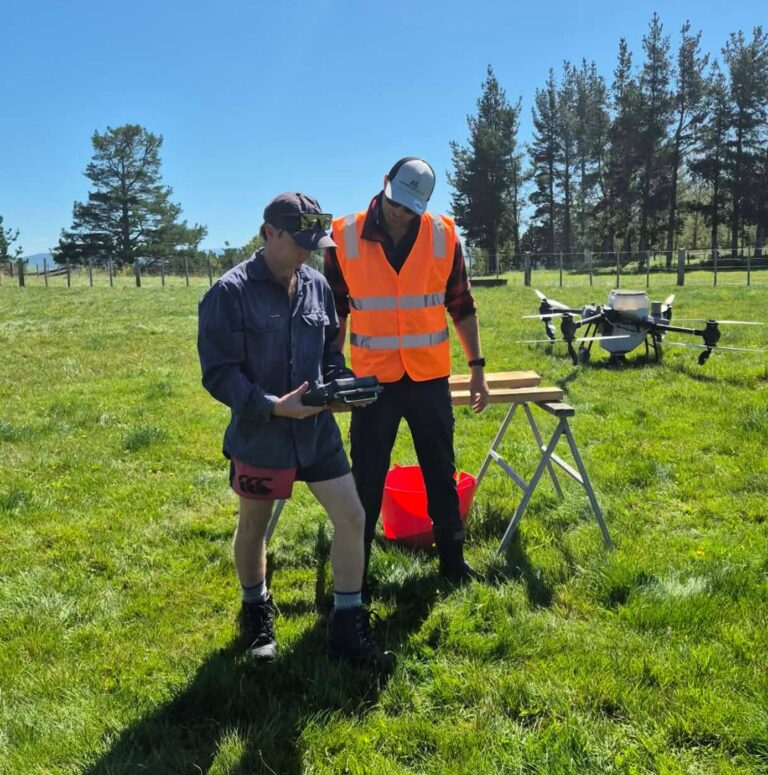 Instructor talking a trainee through the controller beside a spray drone